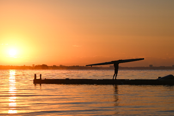 Athlete carying sprint boat off dock after sunrise practice