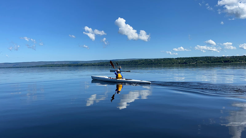 I2C athlete paddling white surfski on a dead flat Saturday morning with clear skies. The sky clearly reflecting in the water.