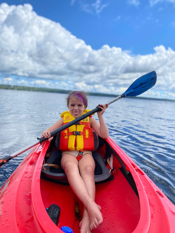 Jr Canoe Kids camper smiling on a beautiful flat day in the back of a red tandem rec kayak